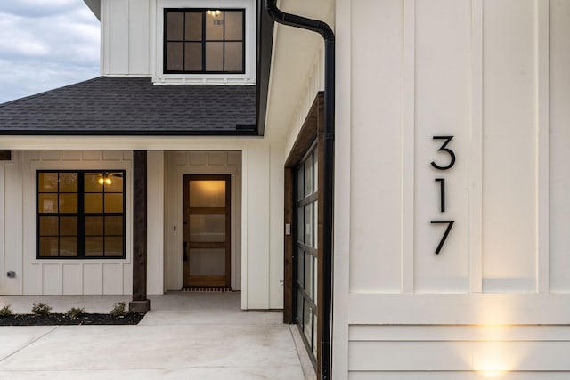 view of exterior entry featuring a shingled roof and board and batten siding