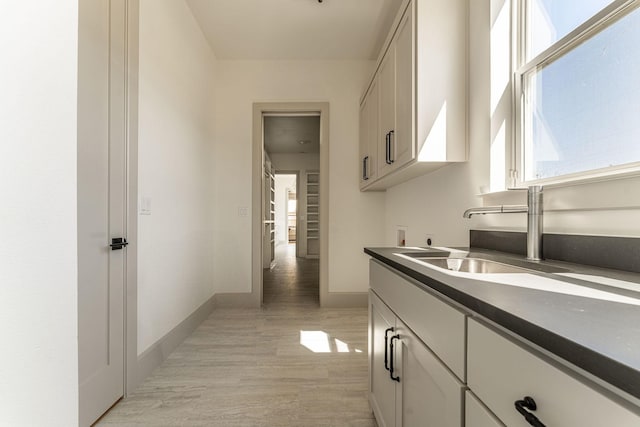 hall featuring baseboards, a sink, and light wood finished floors