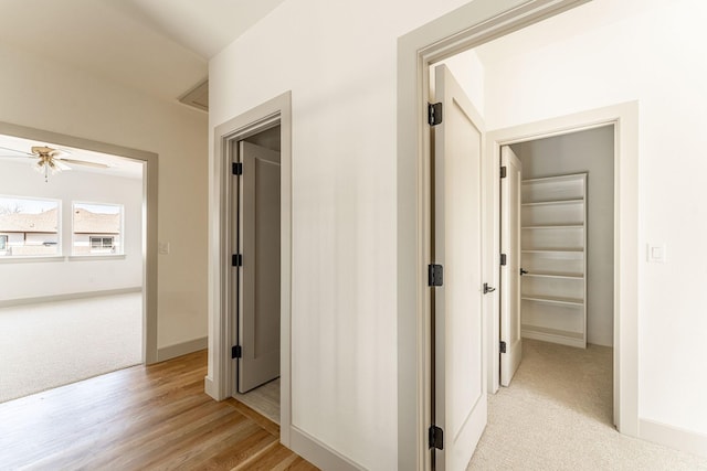 corridor featuring light carpet, light wood-style floors, and baseboards