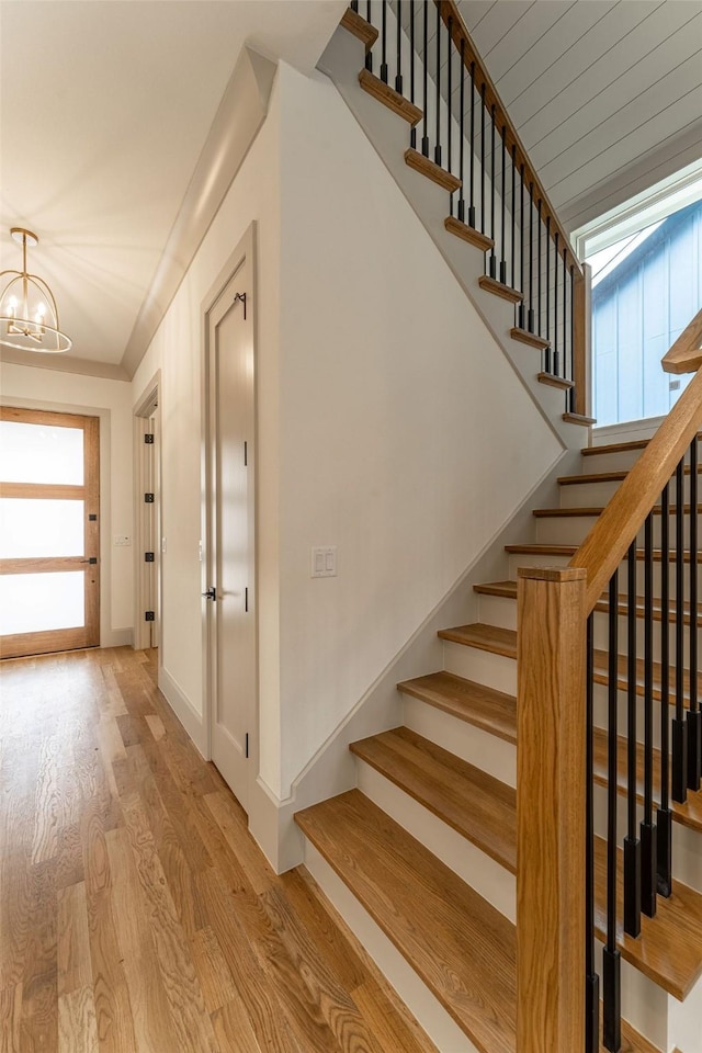 stairway featuring a notable chandelier, baseboards, and wood finished floors