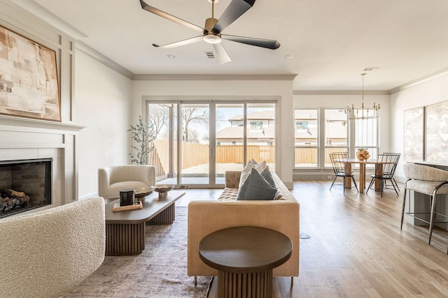 living area featuring visible vents, wood finished floors, crown molding, a fireplace, and ceiling fan with notable chandelier