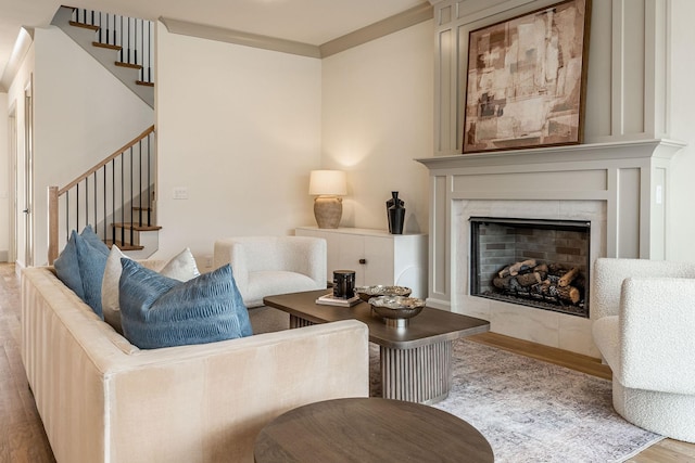 living room with ornamental molding, a tile fireplace, stairway, and wood finished floors