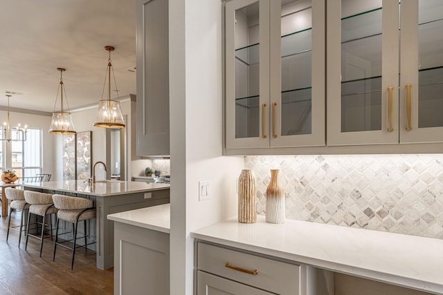 bar with dark wood-style floors, tasteful backsplash, pendant lighting, and a sink