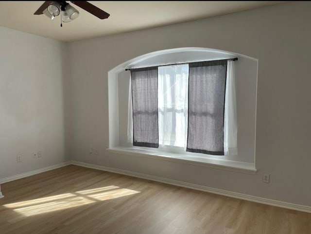 empty room with wood finished floors, a ceiling fan, and baseboards