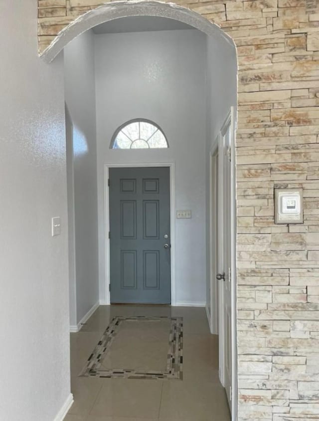 foyer with arched walkways, a high ceiling, baseboards, and tile patterned floors