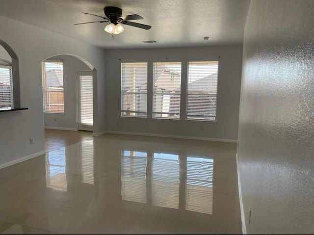 empty room featuring visible vents, a ceiling fan, a textured ceiling, tile patterned flooring, and baseboards