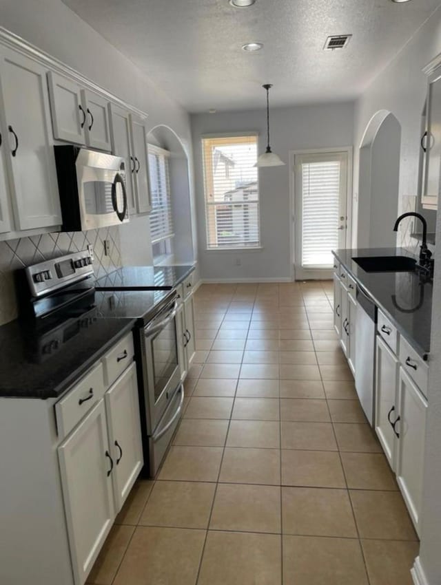 kitchen with light tile patterned floors, stainless steel appliances, visible vents, backsplash, and a sink