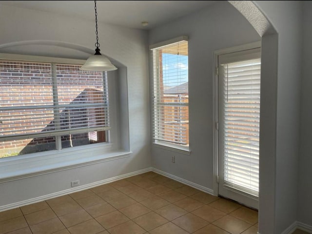 unfurnished dining area with plenty of natural light, tile patterned flooring, and baseboards