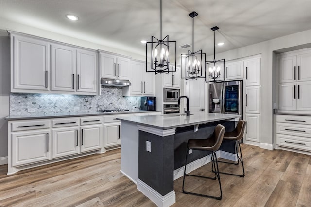 kitchen with stainless steel appliances, light wood-style flooring, visible vents, and under cabinet range hood