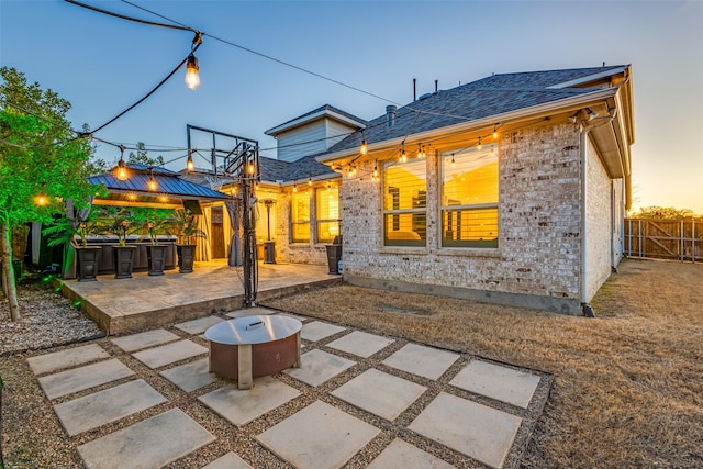 back of house featuring roof with shingles, fence, a gazebo, a patio area, and brick siding