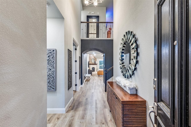 entryway featuring arched walkways, a textured wall, a towering ceiling, wood finished floors, and baseboards