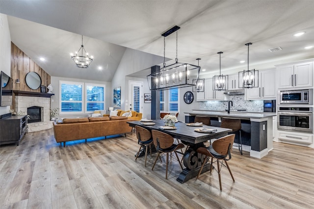 dining room with lofted ceiling, a fireplace, visible vents, light wood-style floors, and an inviting chandelier