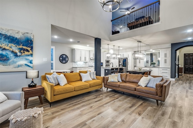 living area featuring arched walkways, a high ceiling, a notable chandelier, and light wood finished floors