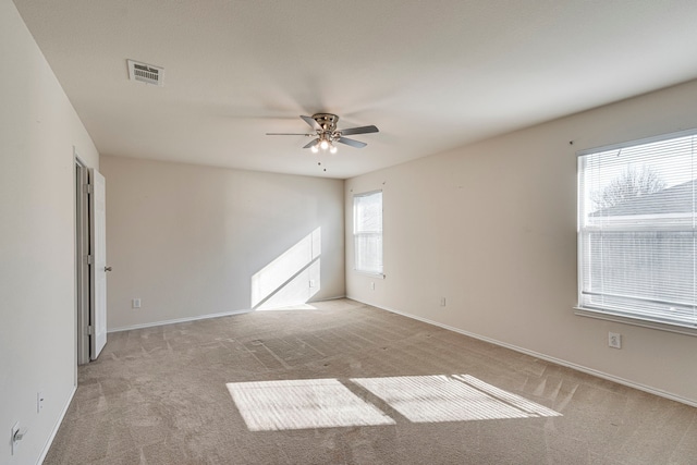 spare room with light carpet, visible vents, baseboards, and a ceiling fan