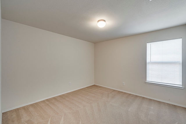 empty room with light carpet, baseboards, and a textured ceiling