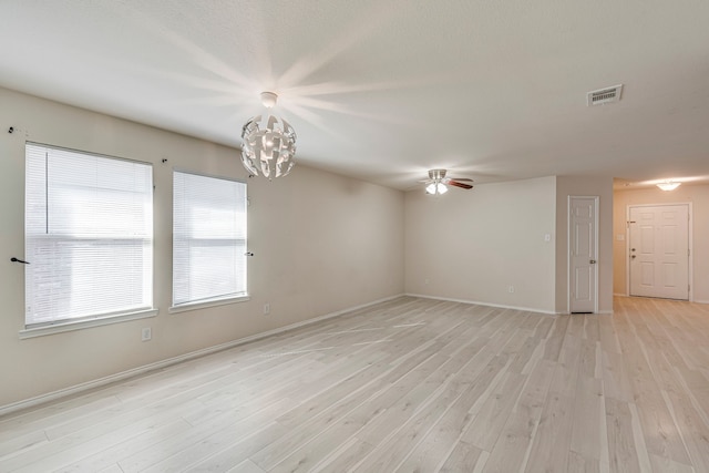 unfurnished room featuring ceiling fan with notable chandelier, light wood-type flooring, visible vents, and baseboards