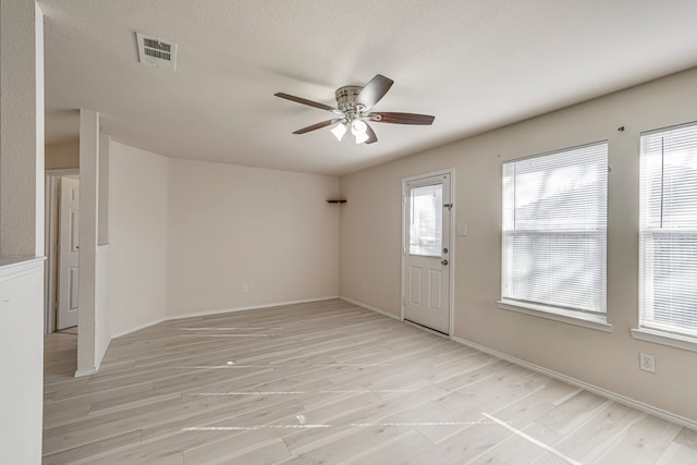 spare room with light wood-type flooring, ceiling fan, visible vents, and a textured ceiling