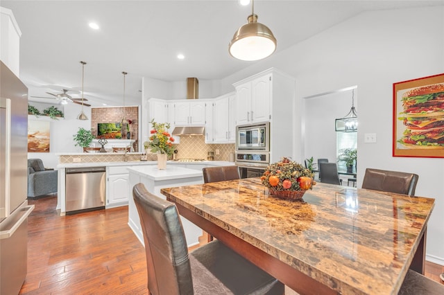 kitchen with dark wood-style flooring, a center island, a peninsula, stainless steel appliances, and under cabinet range hood