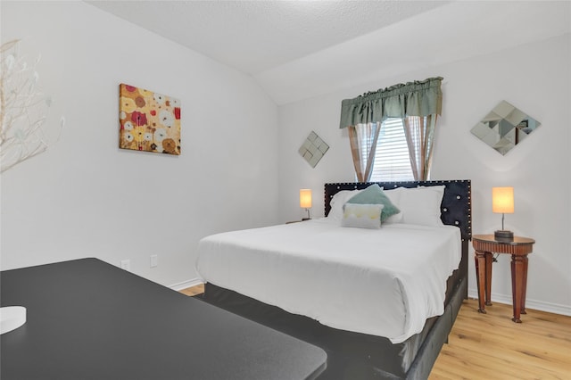 bedroom with light wood-style floors, vaulted ceiling, and baseboards