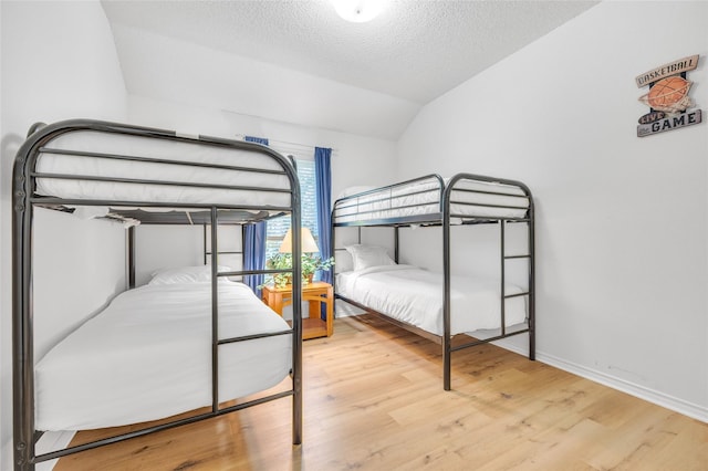 bedroom with lofted ceiling, a textured ceiling, a garage, wood finished floors, and baseboards