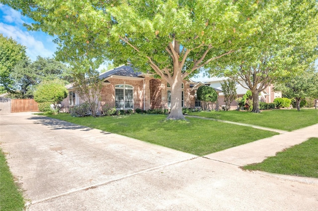 view of front of home featuring concrete driveway, brick siding, fence, and a front lawn