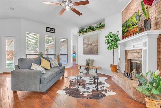 living area with a textured ceiling, wood-type flooring, visible vents, and a brick fireplace