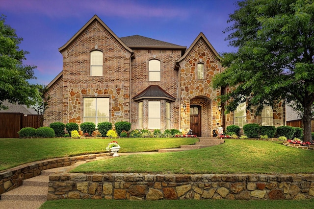 view of front of property featuring fence, stone siding, roof with shingles, brick siding, and a lawn