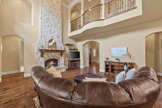 living area featuring arched walkways, a high ceiling, a fireplace, wood finished floors, and baseboards