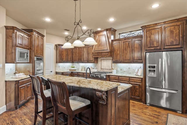 kitchen with appliances with stainless steel finishes, dark wood finished floors, an island with sink, decorative backsplash, and custom exhaust hood