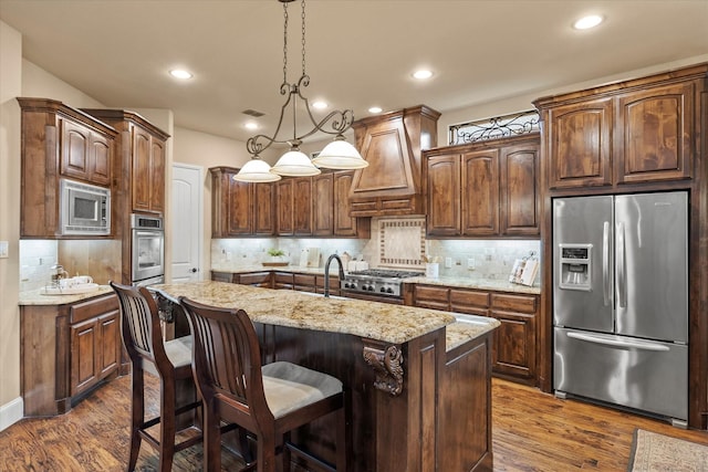 kitchen featuring dark wood finished floors, a center island with sink, stainless steel appliances, custom range hood, and backsplash