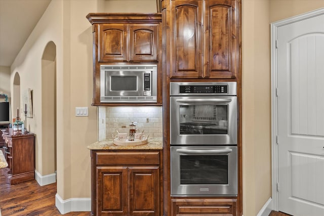 kitchen featuring light stone counters, stainless steel appliances, dark wood-type flooring, baseboards, and backsplash