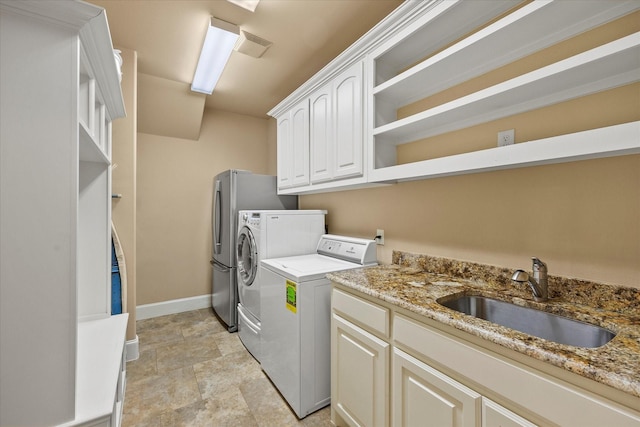 washroom featuring washing machine and dryer, baseboards, stone finish floor, a sink, and cabinet space