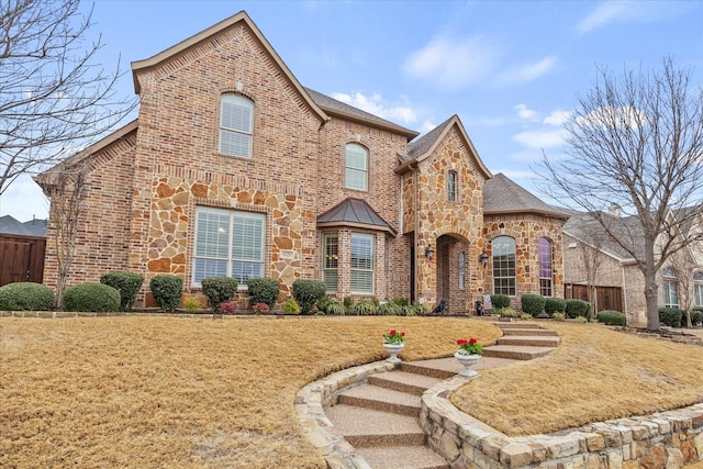 view of front of home featuring stone siding, brick siding, a front yard, and fence