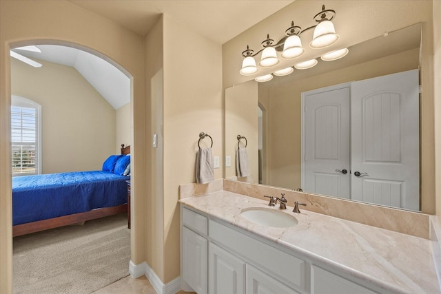 bathroom with vaulted ceiling, vanity, baseboards, and ensuite bathroom