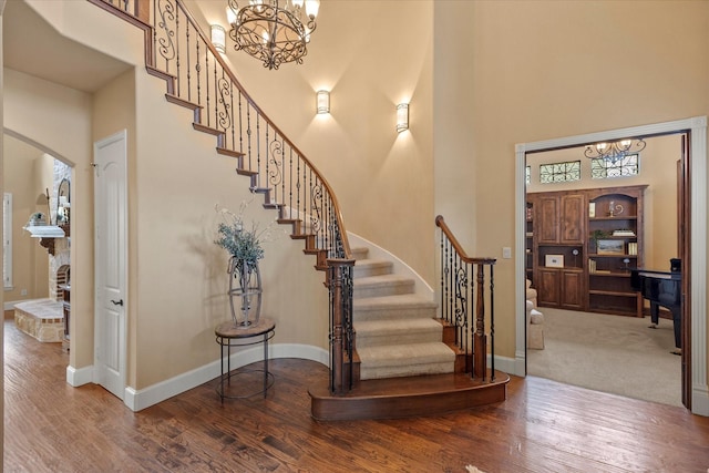 stairs with arched walkways, a notable chandelier, a high ceiling, wood finished floors, and baseboards