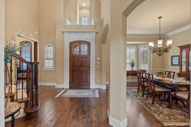 entryway featuring crown molding, baseboards, dark wood-type flooring, a chandelier, and arched walkways