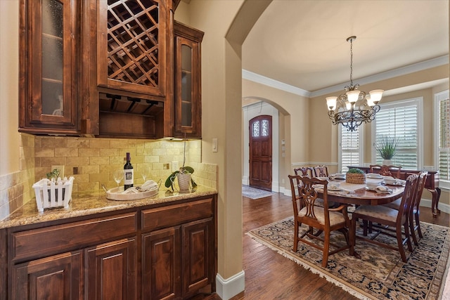 dining area featuring dark wood-style flooring, an inviting chandelier, arched walkways, baseboards, and ornamental molding