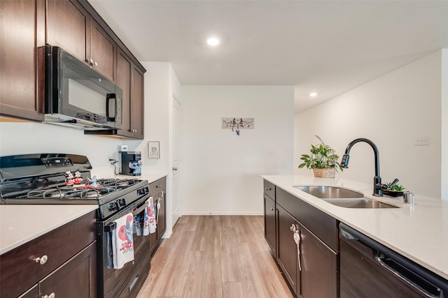 kitchen with dark brown cabinetry, light wood-style flooring, light countertops, black appliances, and a sink