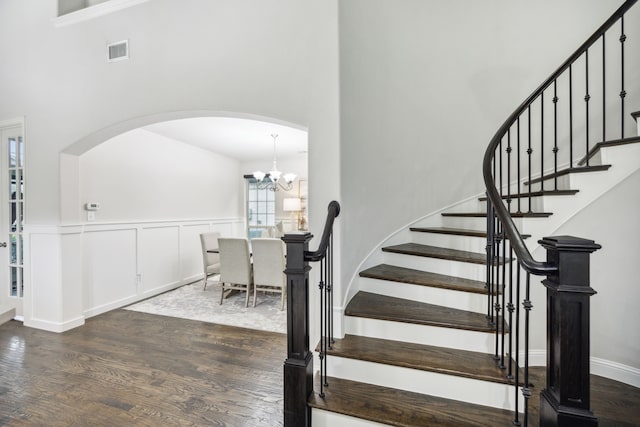 staircase featuring arched walkways, a notable chandelier, wood finished floors, a towering ceiling, and visible vents