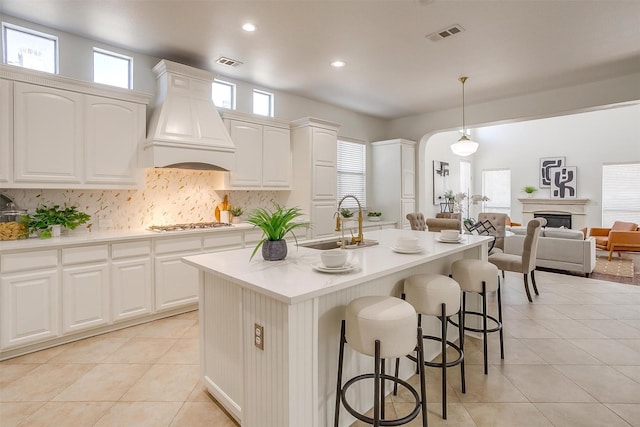 kitchen featuring a kitchen bar, custom range hood, visible vents, and decorative backsplash