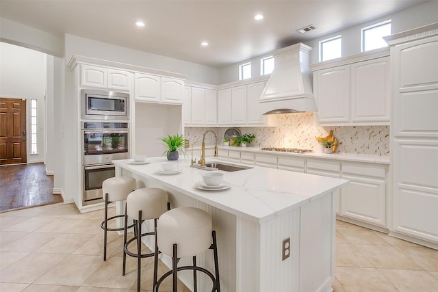 kitchen with stainless steel appliances, a sink, visible vents, custom exhaust hood, and decorative backsplash