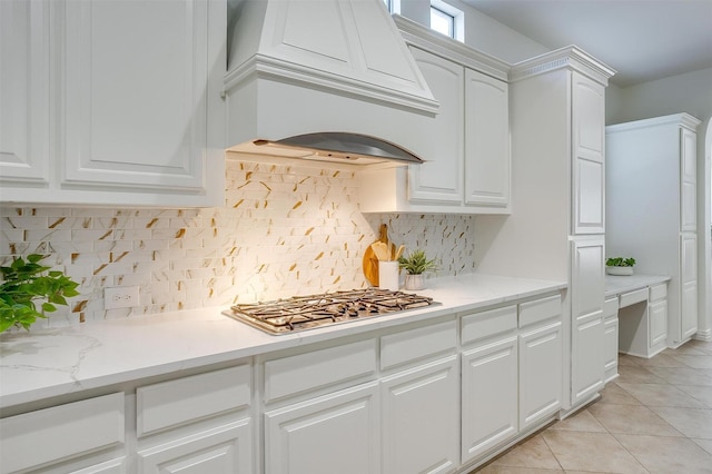 kitchen featuring light tile patterned floors, tasteful backsplash, custom range hood, stainless steel gas stovetop, and white cabinetry