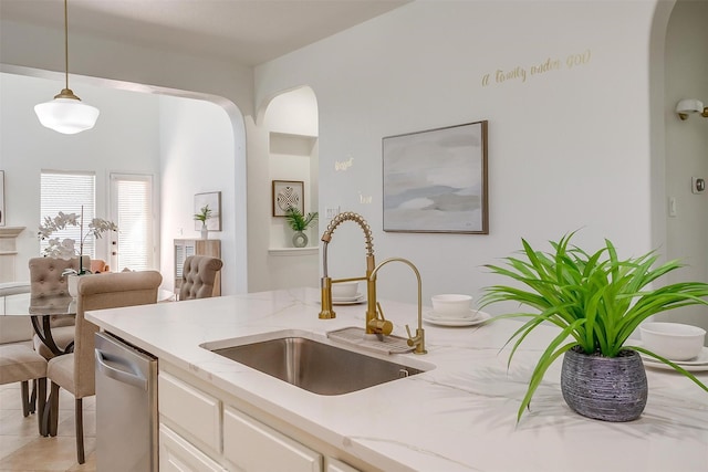 kitchen with arched walkways, light tile patterned floors, a sink, light stone countertops, and dishwasher