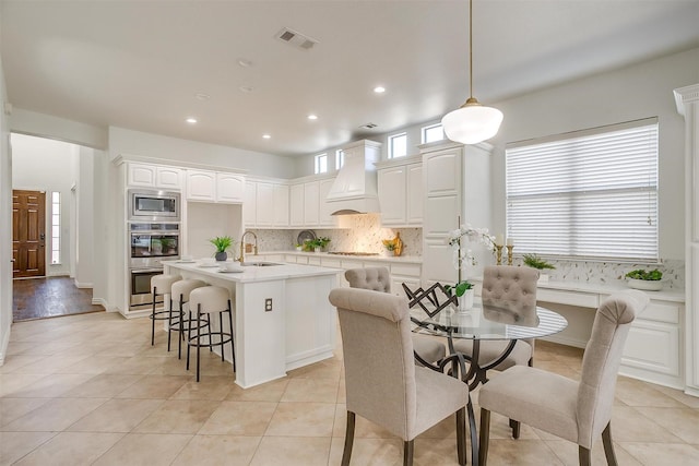 kitchen with tasteful backsplash, visible vents, custom exhaust hood, stainless steel appliances, and a sink