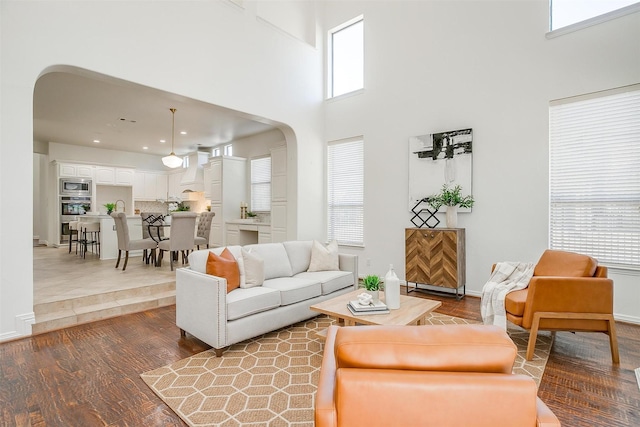 living room featuring arched walkways, recessed lighting, a high ceiling, wood finished floors, and baseboards