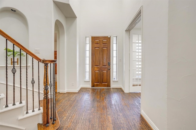 entrance foyer with stairway, baseboards, arched walkways, and wood finished floors