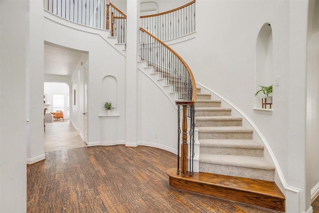 staircase with arched walkways, baseboards, a high ceiling, and wood finished floors