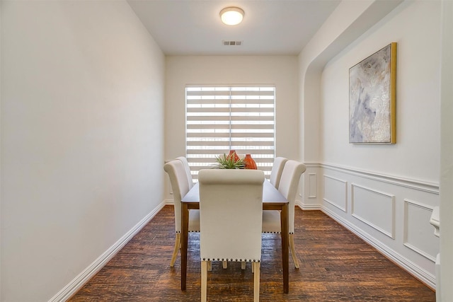 dining area with visible vents, a decorative wall, baseboards, and wood finished floors