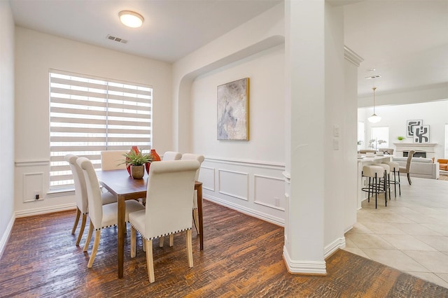 dining space featuring wainscoting, a decorative wall, visible vents, and wood finished floors