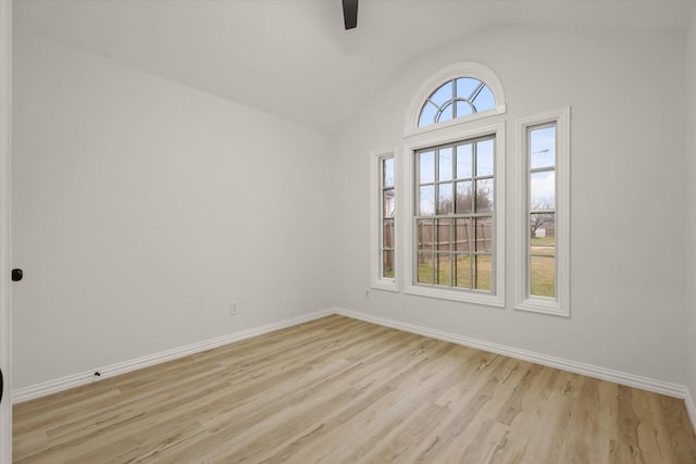 spare room with baseboards, vaulted ceiling, and light wood finished floors